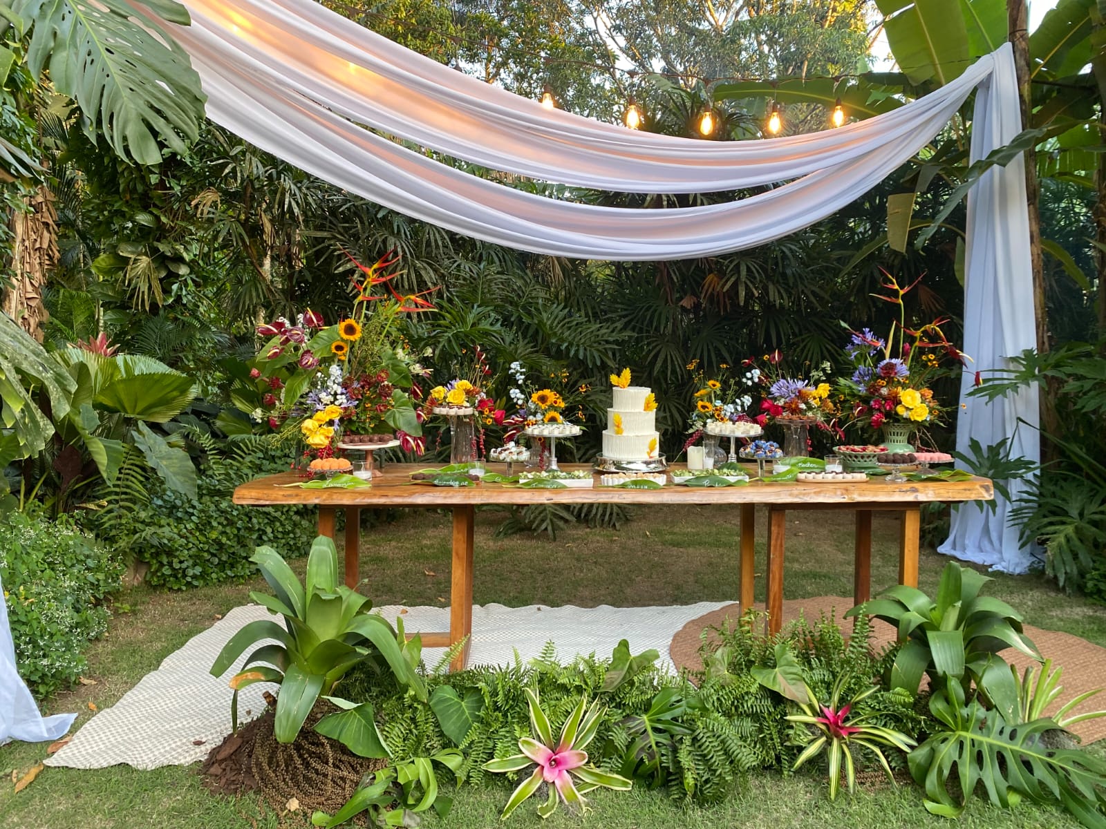 Mesa de bolo com flores tropicais e tecido suspenso